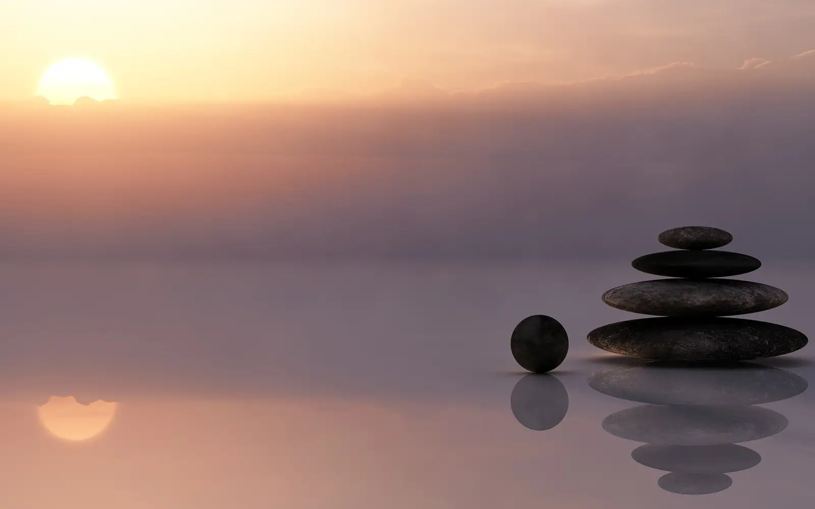 Smooth black stones stacked beside calm water under a soft pink sky