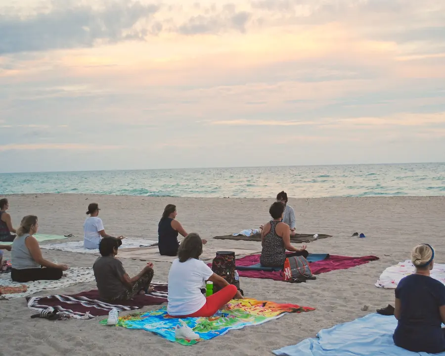Group meditating on colorful blankets on a beach at dusk