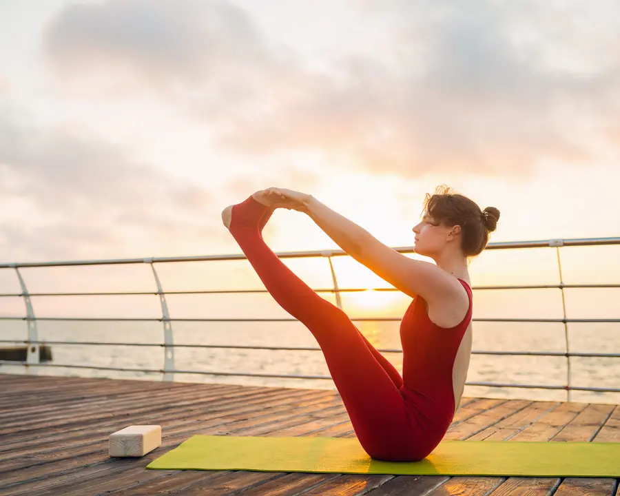 Woman balancing in boat pose on a seaside deck at sunrise