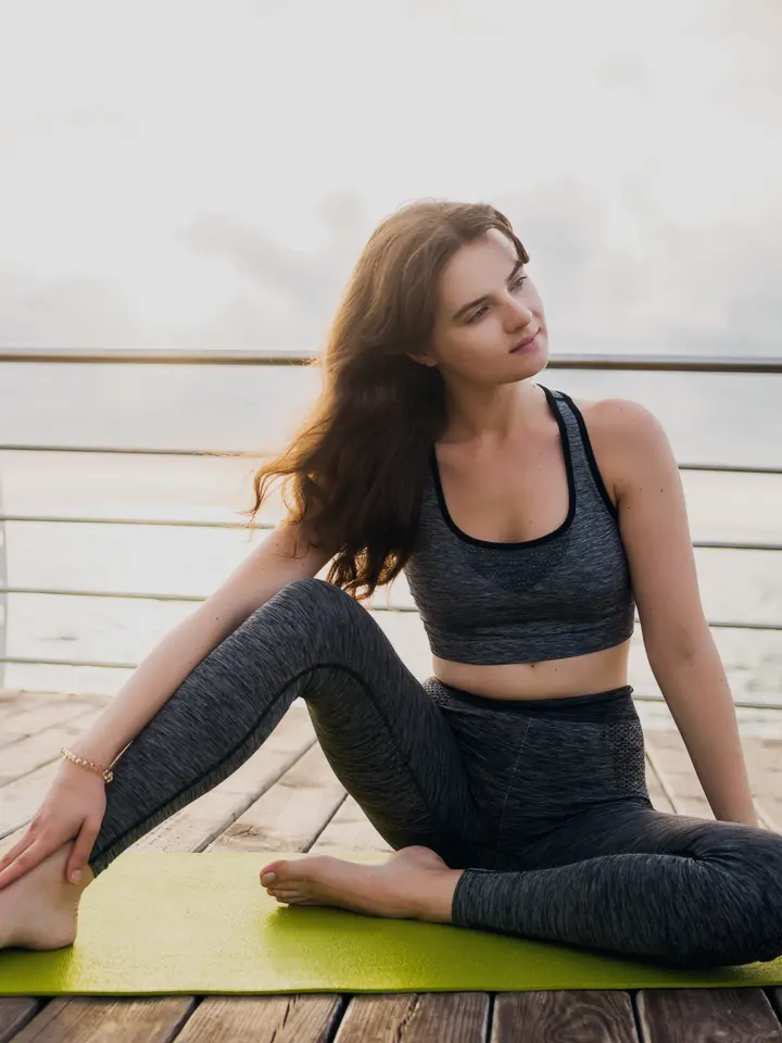 Maya Collins seated in a gentle twist on a mat by the sea