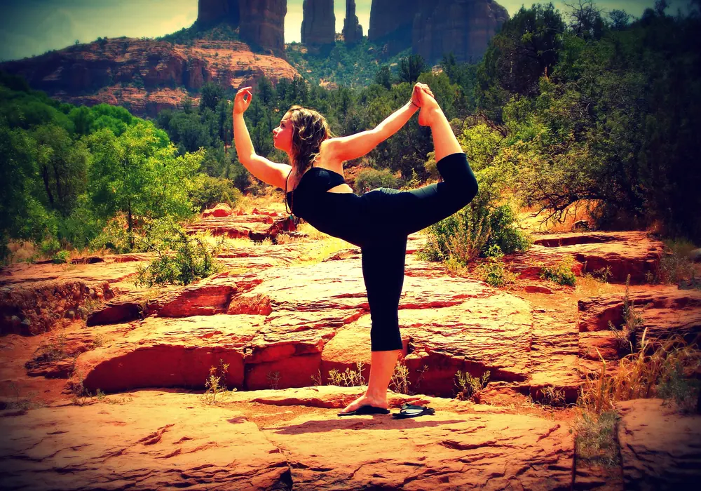 Woman in dancer pose on red rocks in a desert canyon
