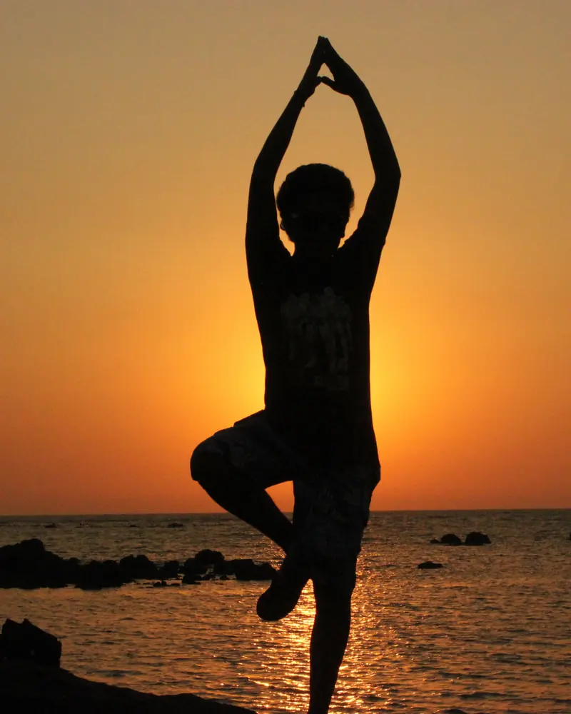 Silhouette in tree pose with arms raised against an orange sunset