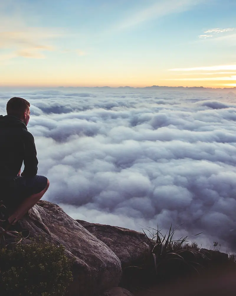 Person sitting on a rocky summit above a sea of clouds