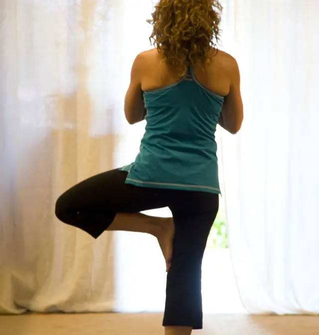 Woman balancing in tree pose on a mat in a softly lit room